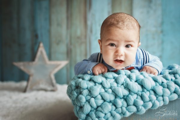 Sedinta foto de bebelus cu Radu in studio, bebelus pe burta pe paturica impletita albastra pe fundal de lemn albastru